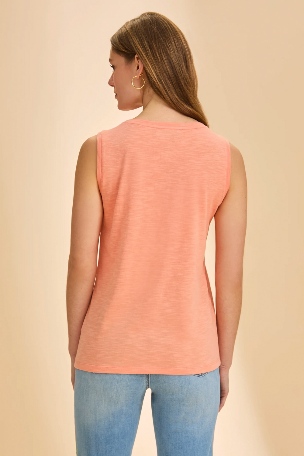 Woman wearing a peach sleeveless top and blue jeans against a beige background