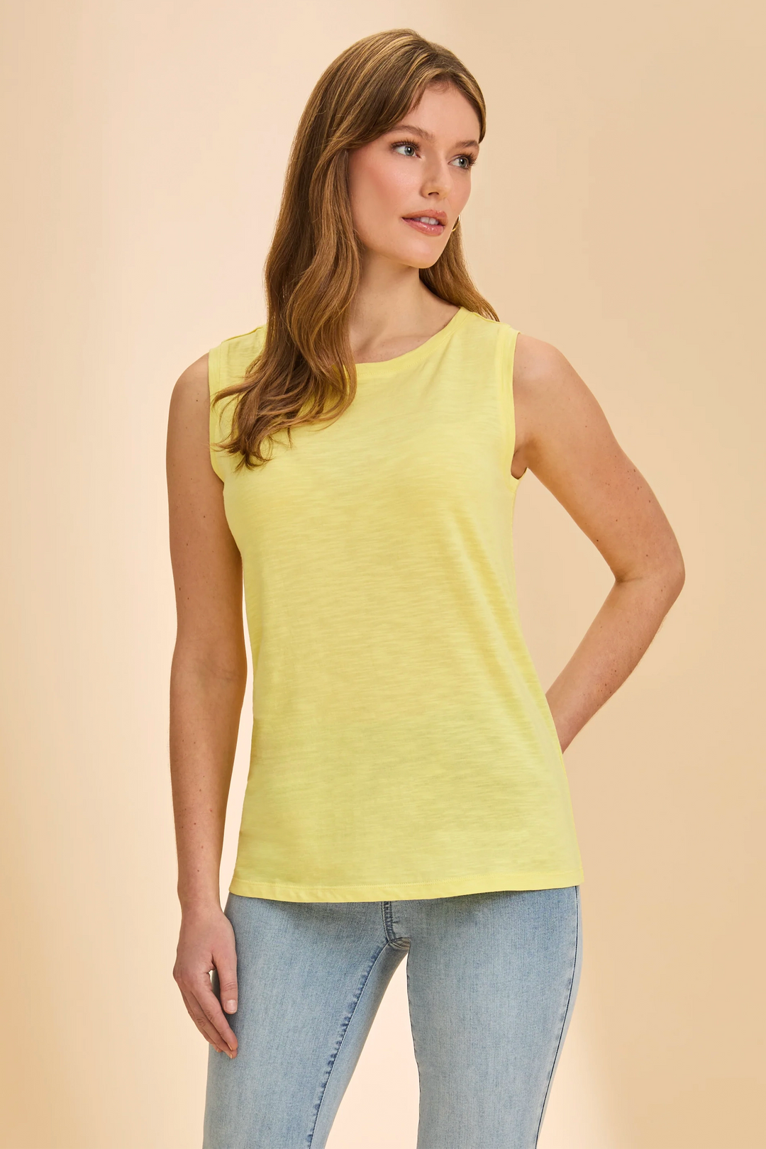 Woman wearing a yellow sleeveless top and blue jeans on a beige background