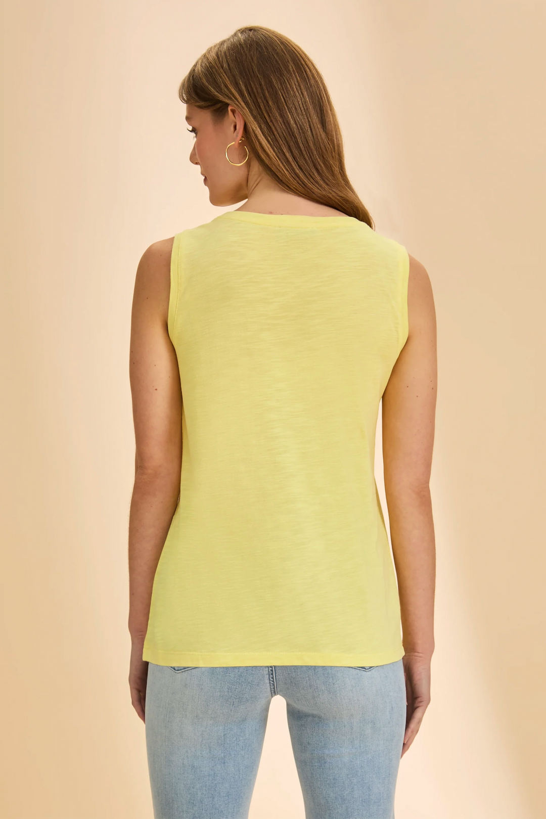 Woman wearing a yellow sleeveless top and blue jeans on a beige background