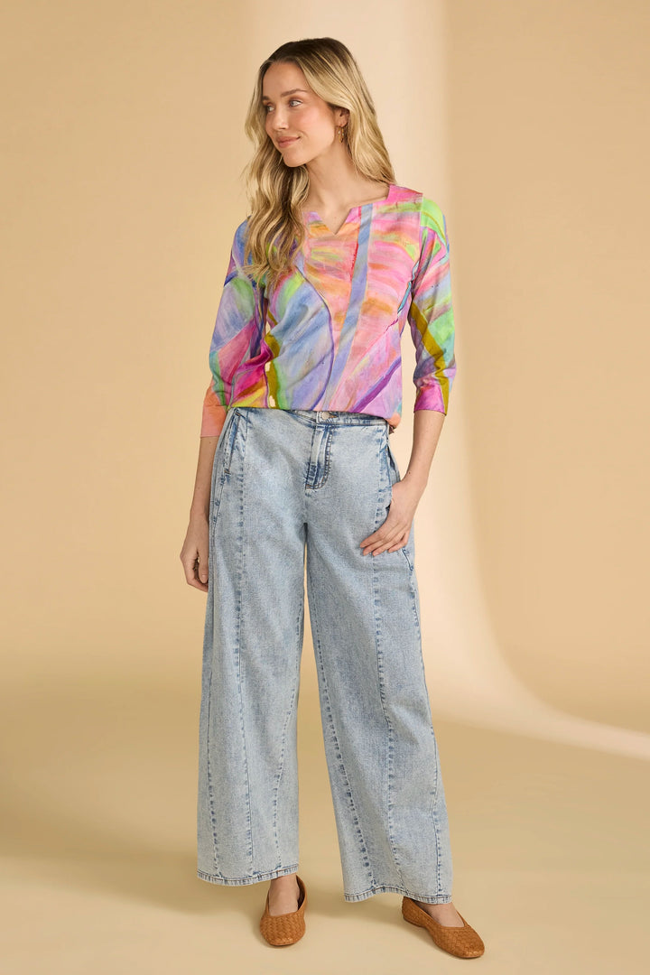 Woman wearing a colorful tie-dye shirt and light blue jeans on a beige background