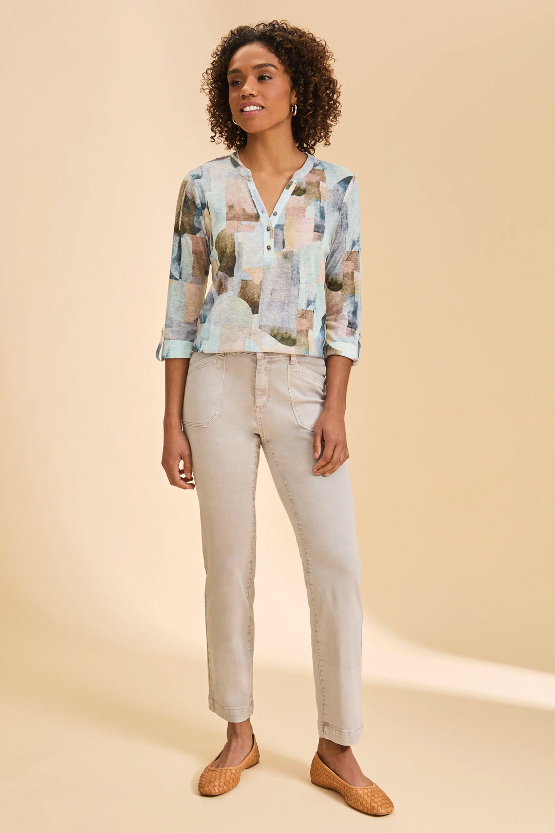 Woman wearing a patterned blouse and light-colored pants on a beige background