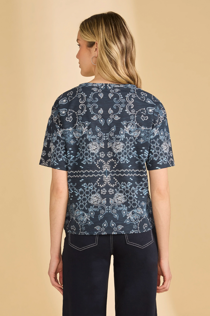 Woman wearing a navy patterned top and black pants on a beige background
