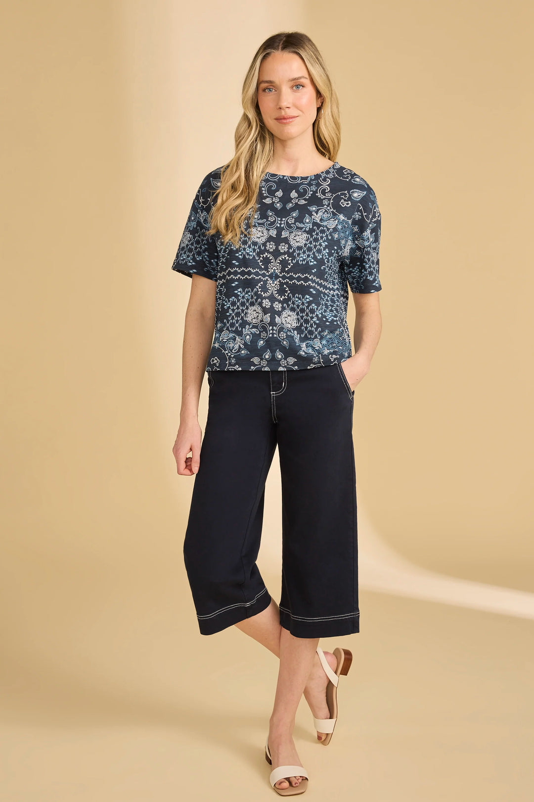 Woman wearing a navy patterned top and black capri pants on a beige background