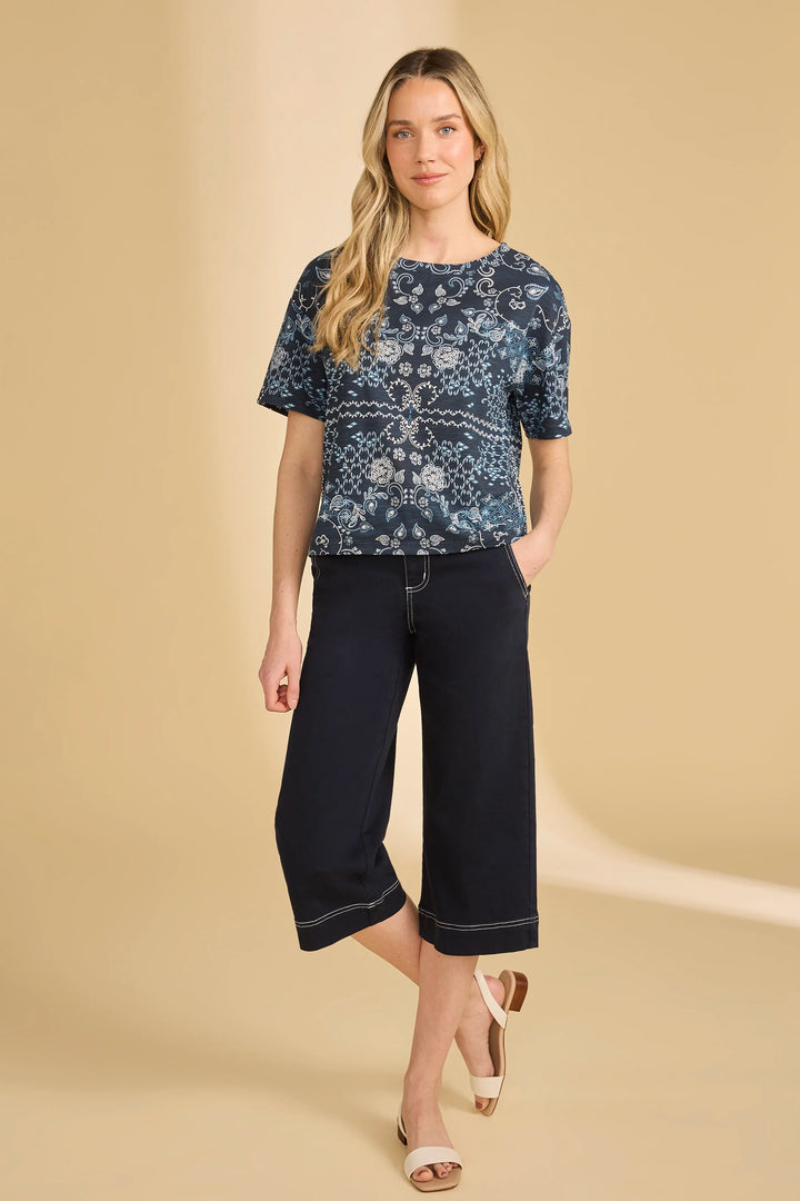 Woman wearing a navy patterned top and black capri pants on a beige background