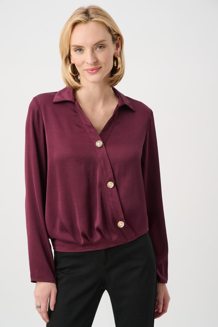 Woman wearing a burgundy silky blouse with gold buttons on a white background