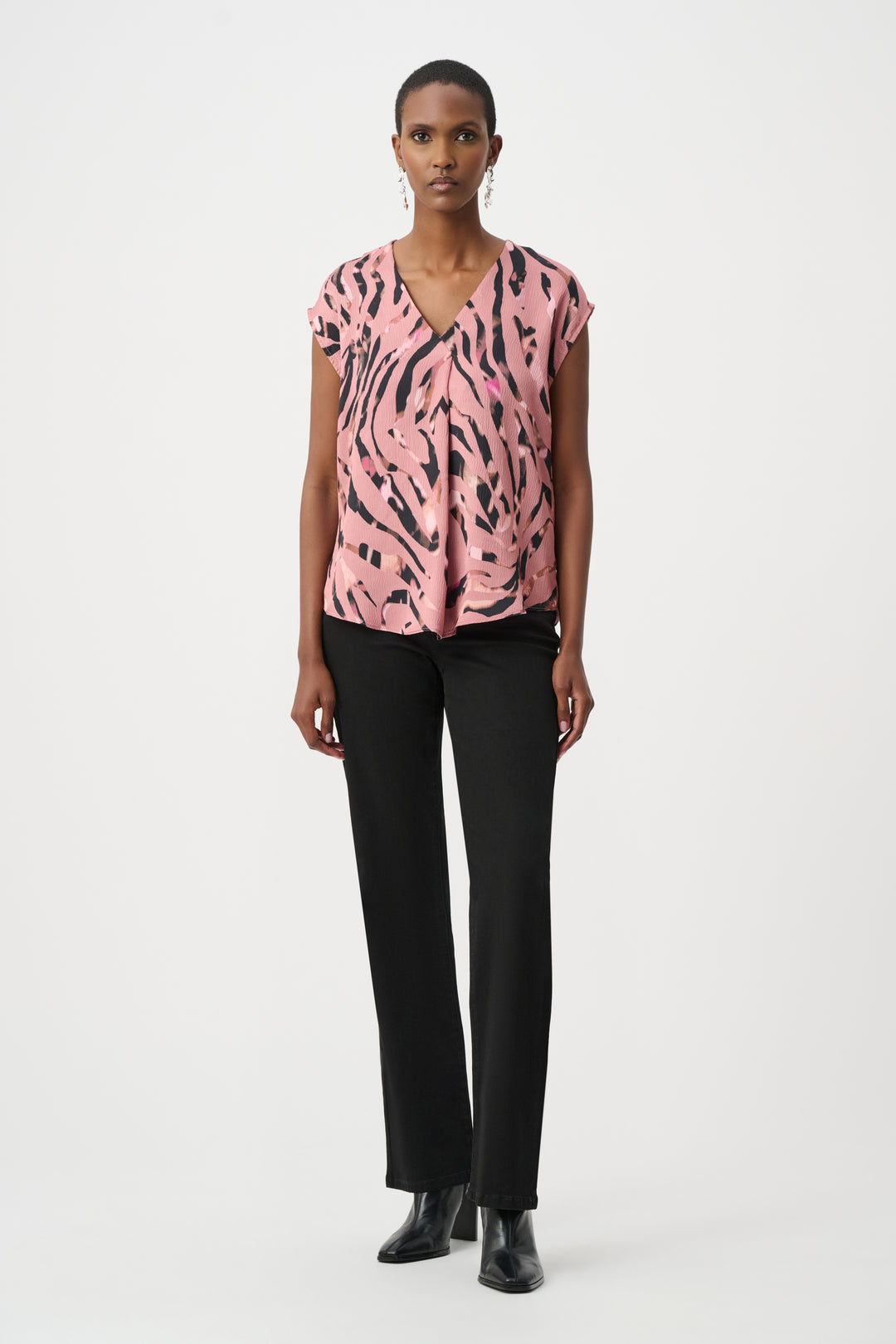 Woman wearing a pink patterned top and black pants on a white background