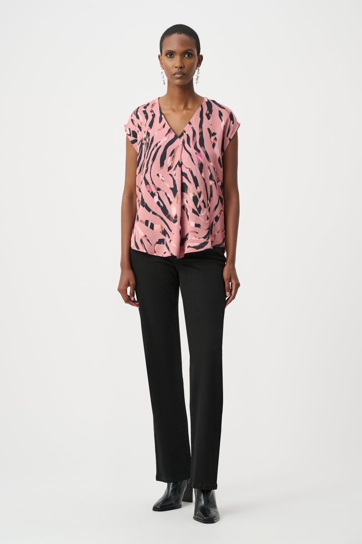 Woman wearing a pink patterned top and black pants on a white background