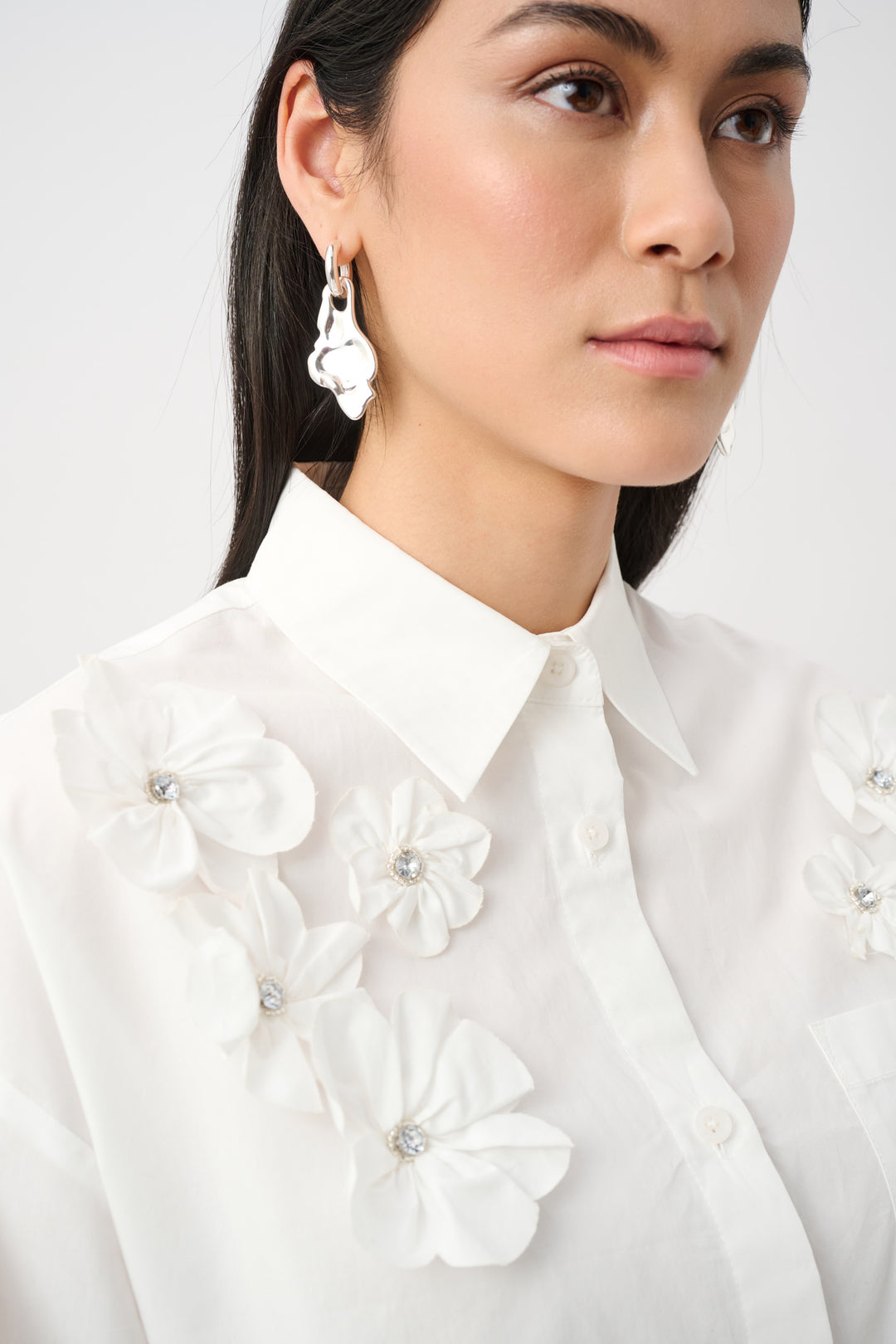 Woman wearing a white blouse with floral embellishments on a plain background