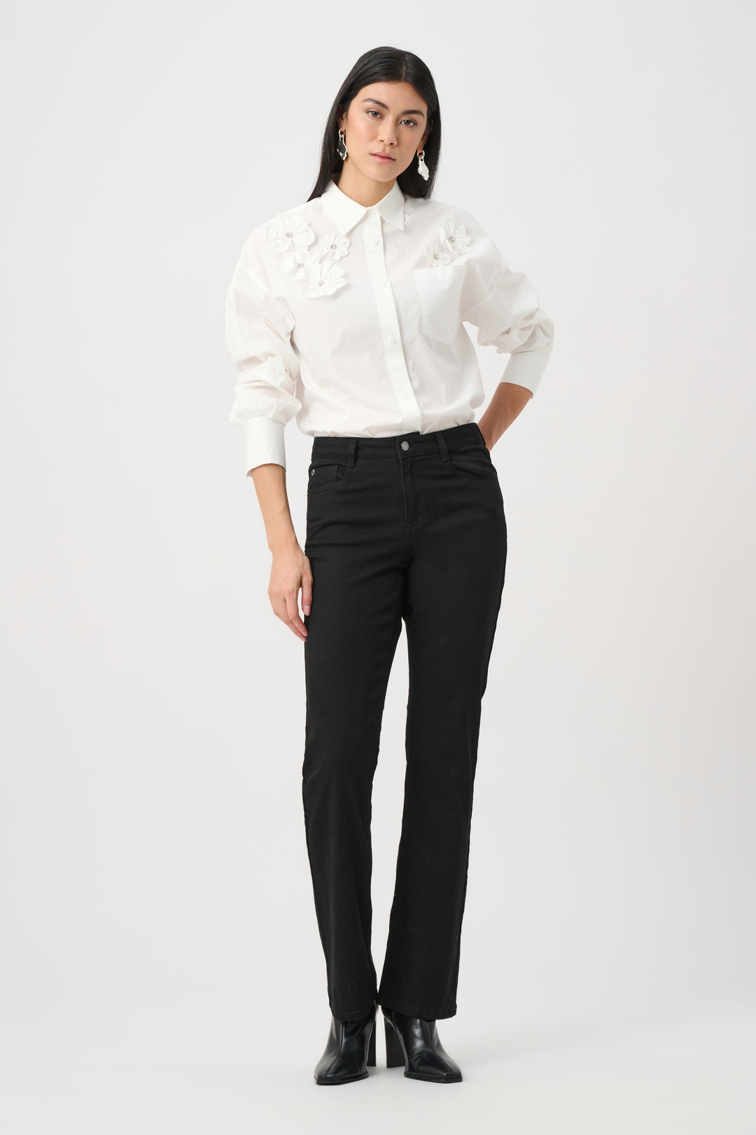 Woman wearing a white blouse with ruffled details and black pants on a white background
