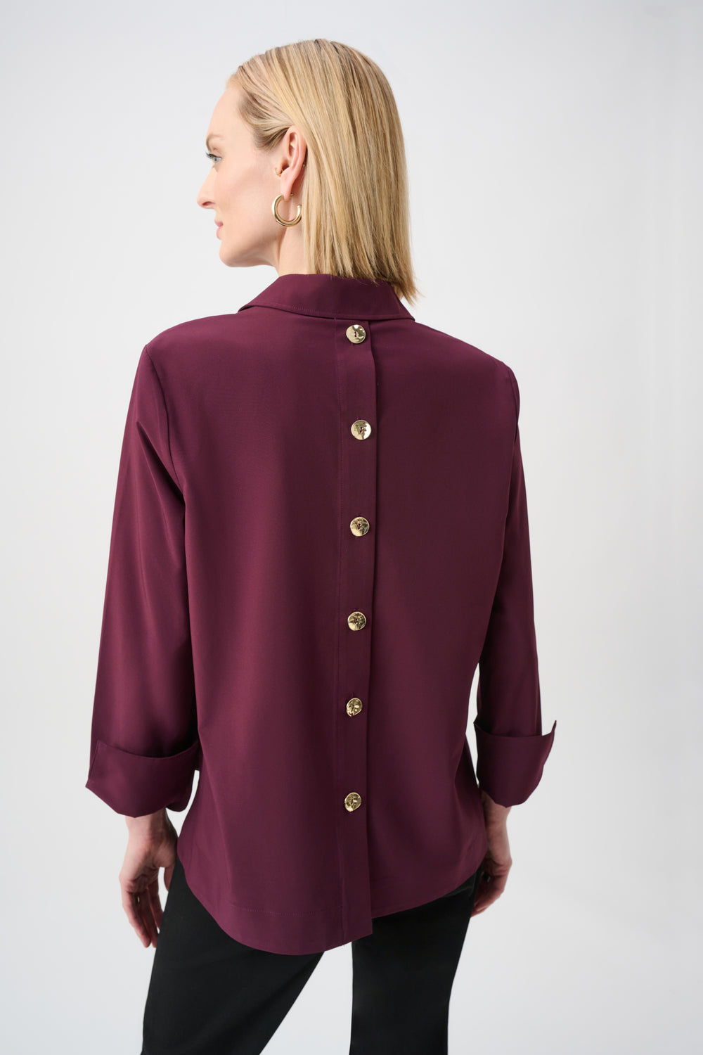 Woman wearing a burgundy blouse with gold buttons on a white background