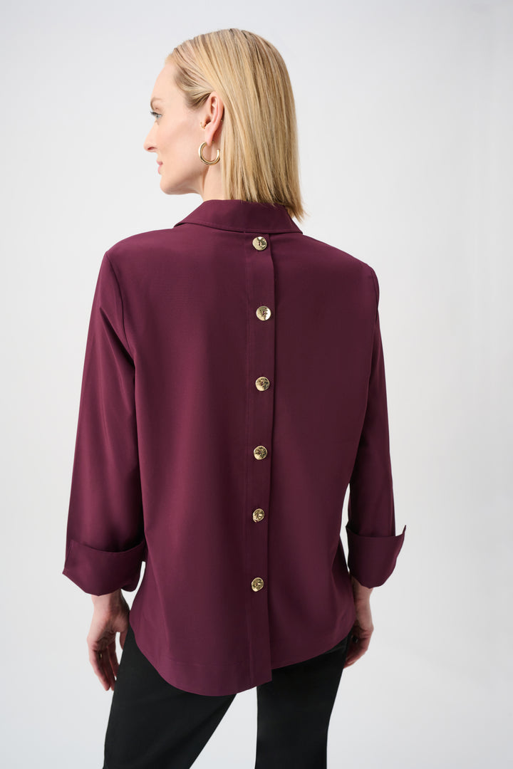 Woman wearing a burgundy blouse with gold buttons on a white background