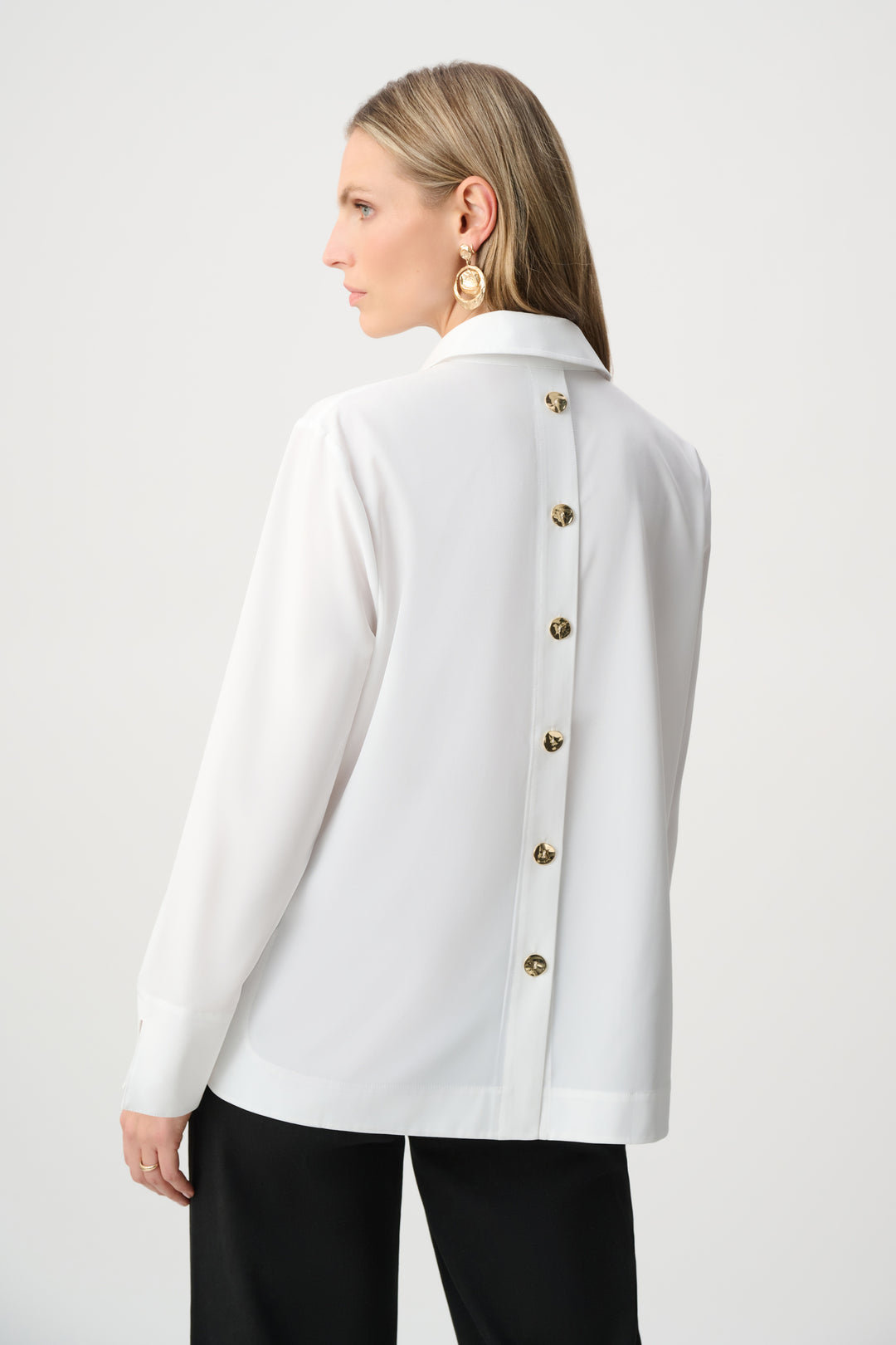Woman wearing a white jacket with gold buttons on a plain background