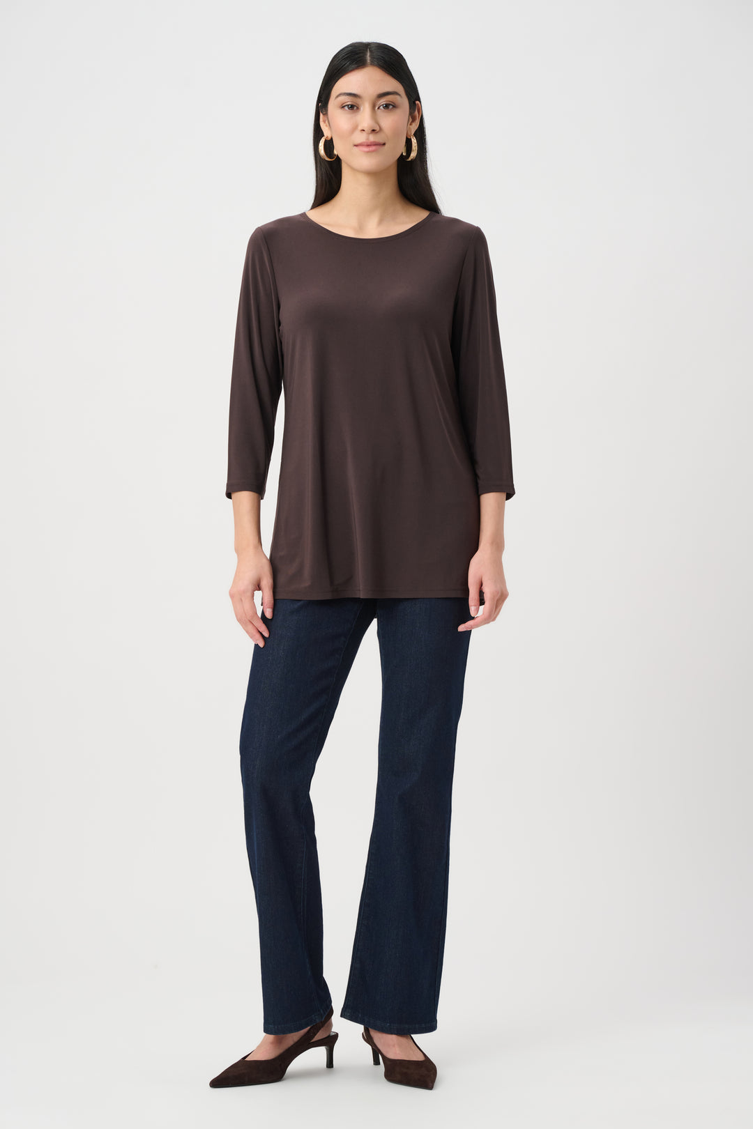Woman wearing a brown long-sleeve top and dark blue pants on a white background