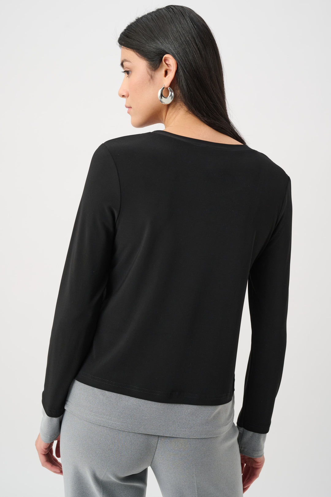 Woman wearing a black long-sleeve top and gray pants on a white background