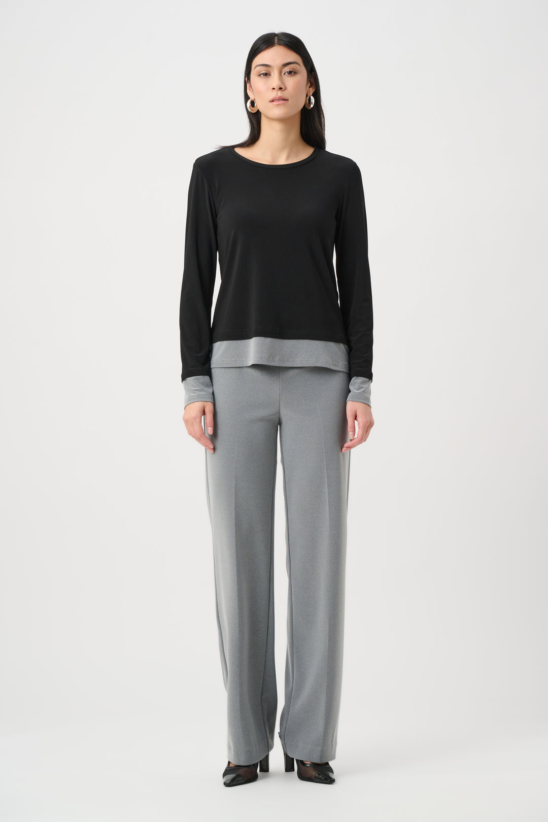 Woman wearing a black long-sleeve top and gray pants on a white background