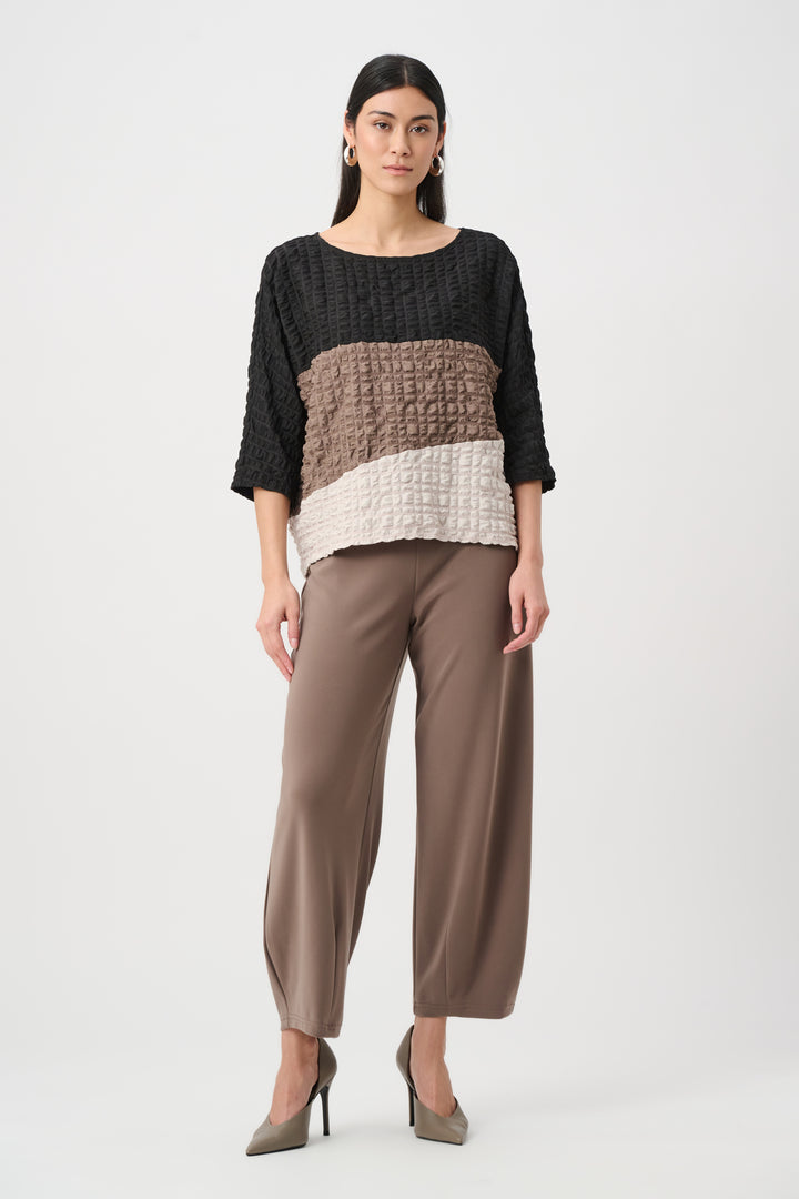 Woman wearing a black, brown, and white top with brown pants on a white background