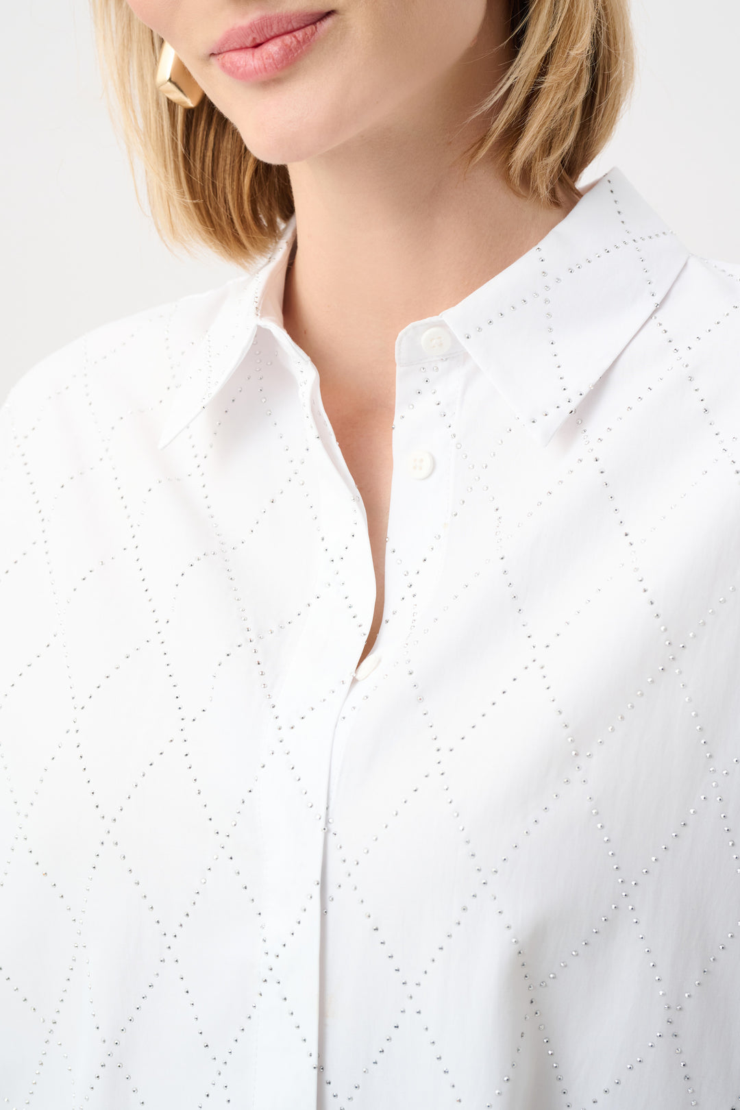 Close-up of a person wearing a white blouse with a subtle pattern on a plain background