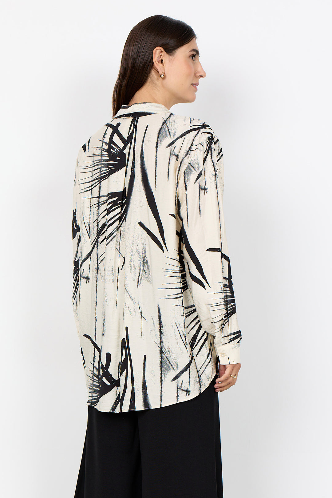 Woman wearing a cream blouse with abstract print and black pants on a white background. 