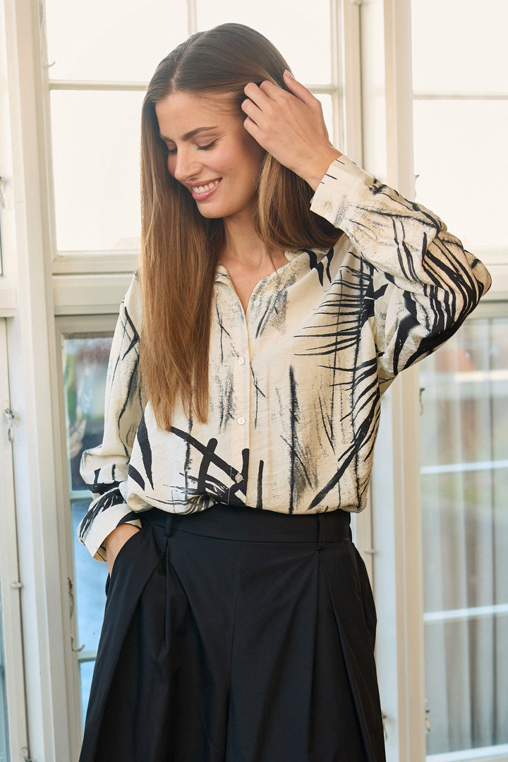 Woman wearing a cream blouse with abstract print in front of a bright window