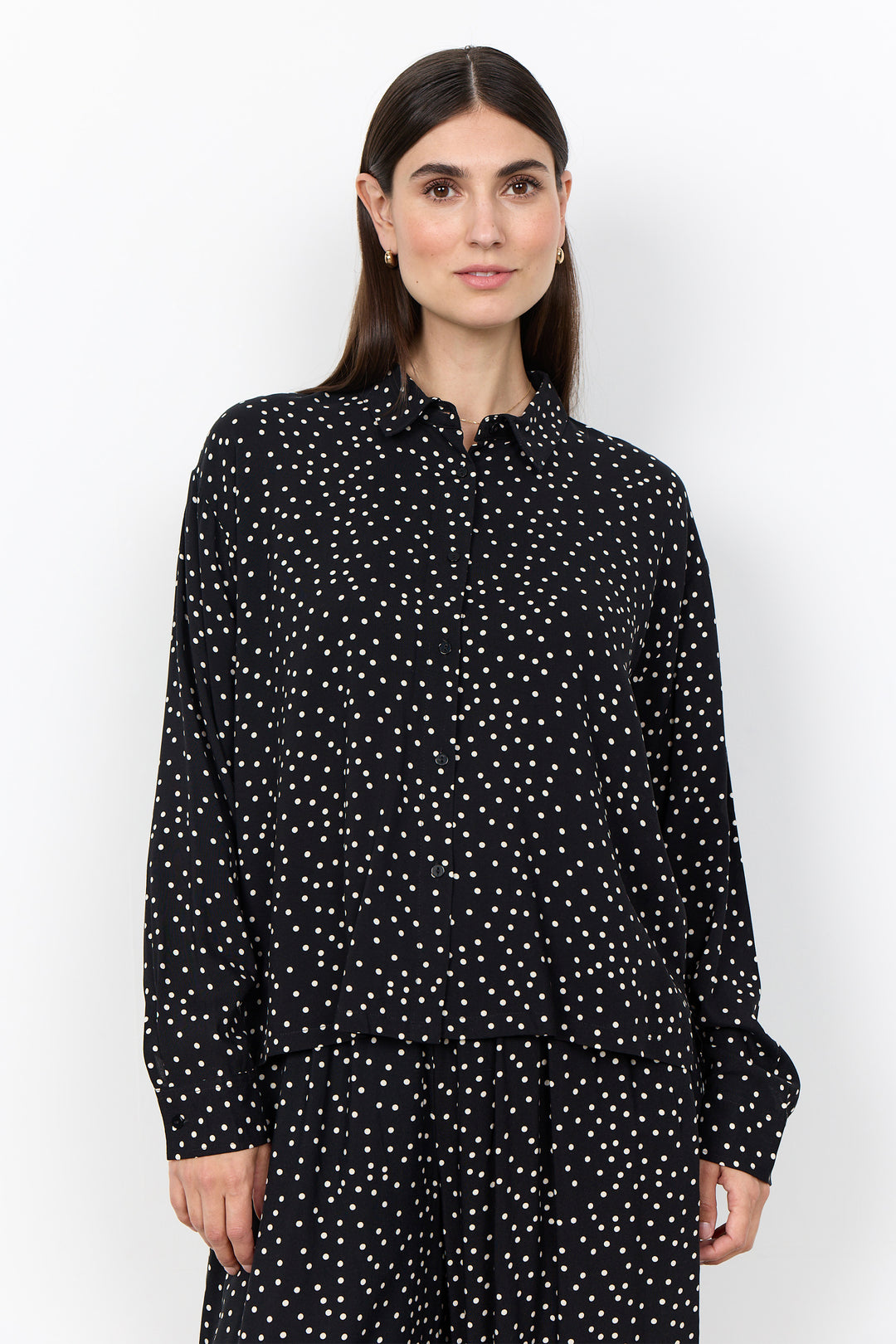 woman wearing a black blouse with white polka dots and matching pants on a white background. 