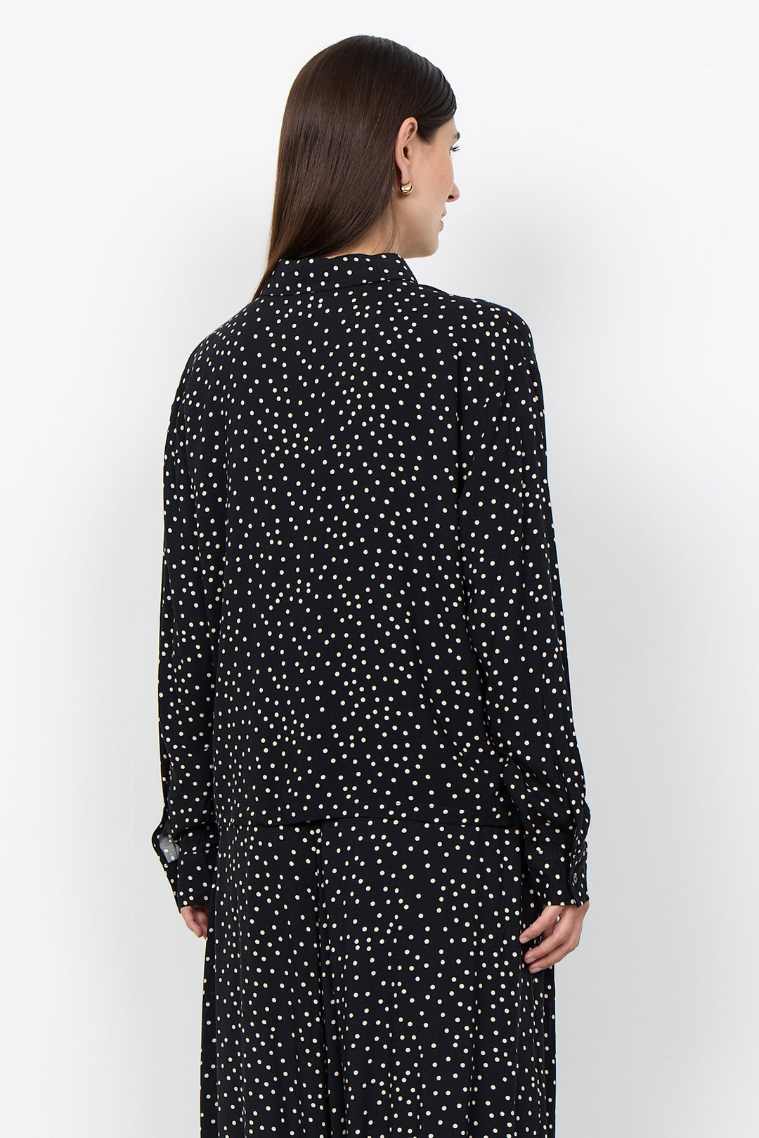 woman wearing a black blouse with white polka dots and matching pants on a white background. 