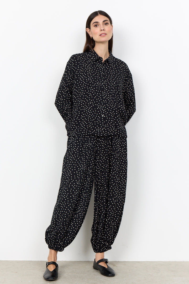 woman wearing a black blouse with white polka dots and matching pants on a white background. 