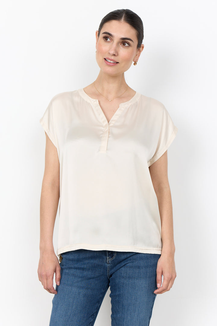 woman wearing a silk t-shirt blouse and jeans on a white background. 