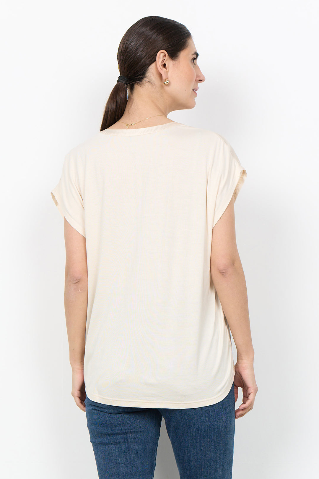 woman wearing a silk t-shirt blouse and jeans on a white background. 