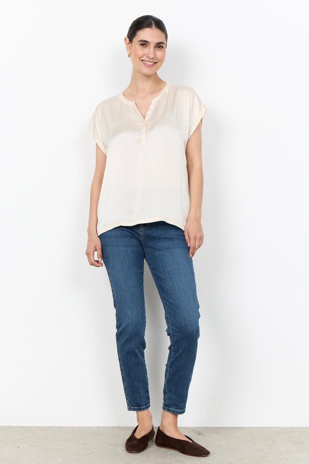 woman wearing a silk t-shirt blouse and jeans on a white background. 