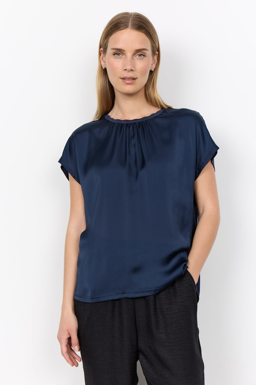 woman wearing a silk t-shirt style blouse with black pants on a white background. 