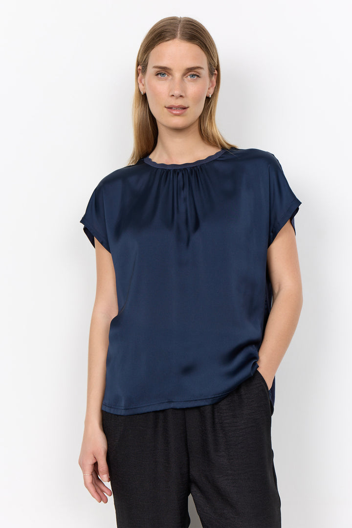 woman wearing a silk t-shirt style blouse with black pants on a white background. 