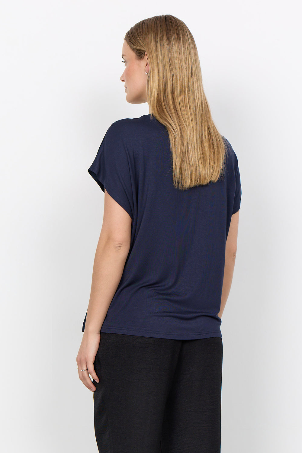 woman wearing a silk t-shirt style blouse with black pants on a white background. 