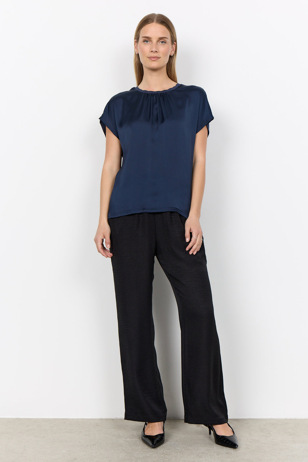 woman wearing a silk t-shirt style blouse with black pants on a white background. 