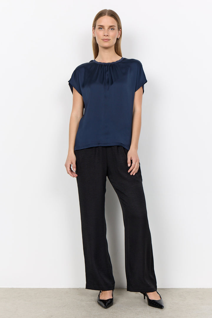 woman wearing a silk t-shirt style blouse with black pants on a white background. 