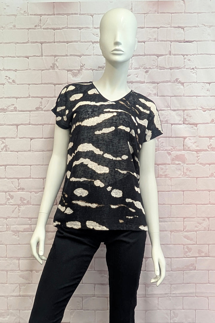A black short-sleeve V-neck top with a beige abstract wavy pattern, displayed on a white female mannequin against a light pink brick wall backdrop.