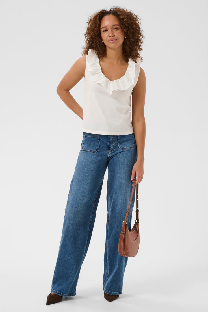 A woman modeling a white sleeveless ruffled top and wide-leg blue jeans, holding a brown shoulder bag against a clean white studio background.