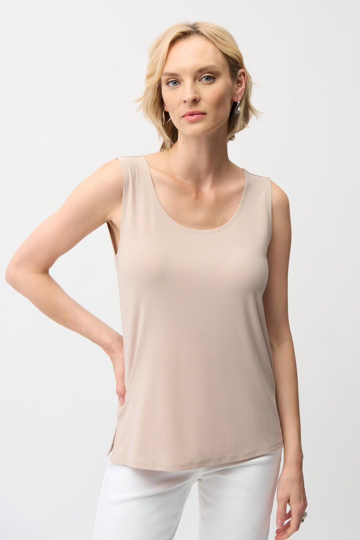 Woman wearing a beige tank top and white pants on a light gray background