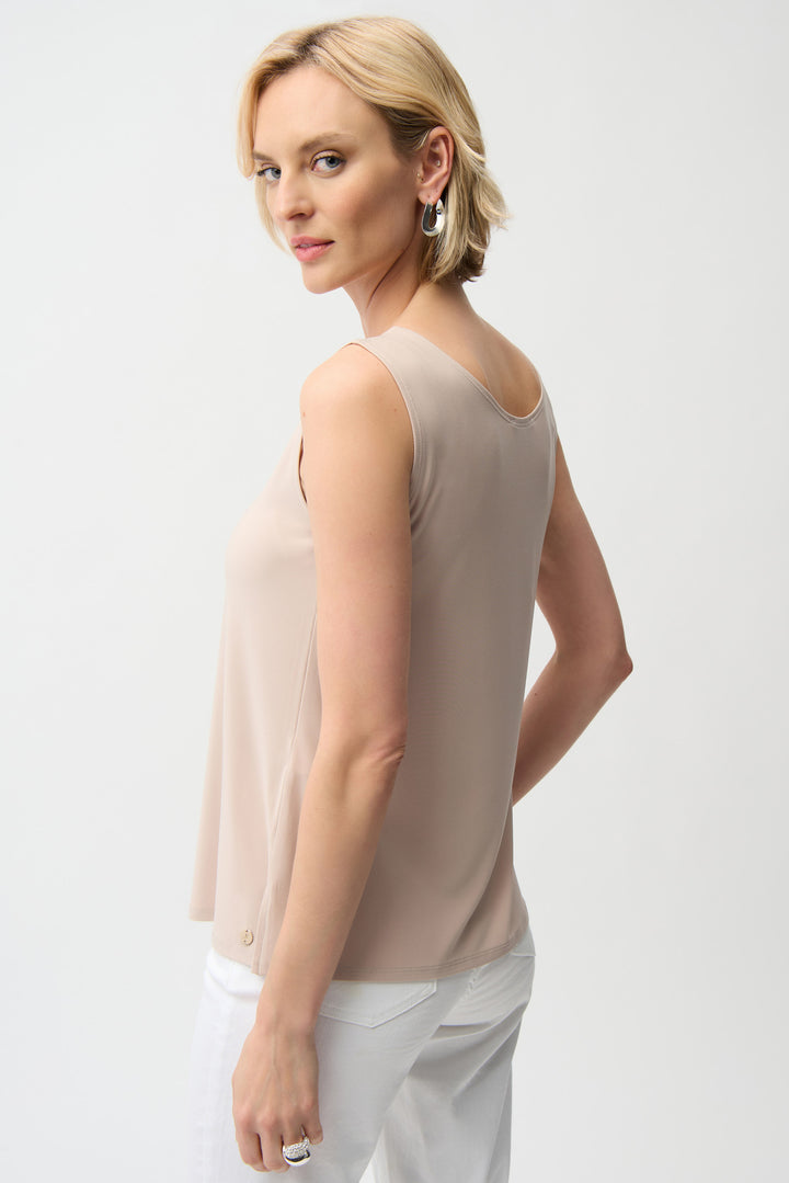 Woman wearing a beige sleeveless top and white pants on a light gray background