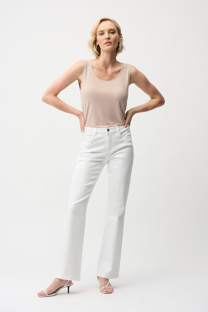 Woman wearing a beige tank top and white pants on a white background