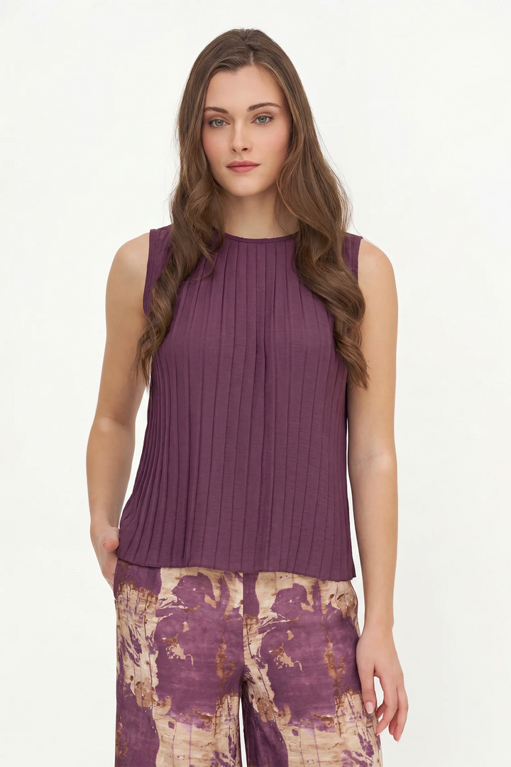 A woman modeling a sleeveless, ribbed purple top with a high round neckline, paired with patterned pants, against a plain white studio background.