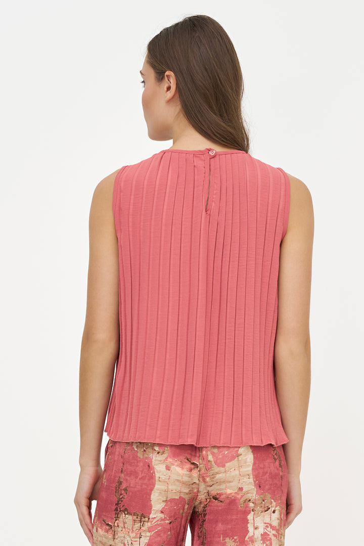 A woman shown from the back wearing a sleeveless pink pleated top and patterned pants against a plain light background.