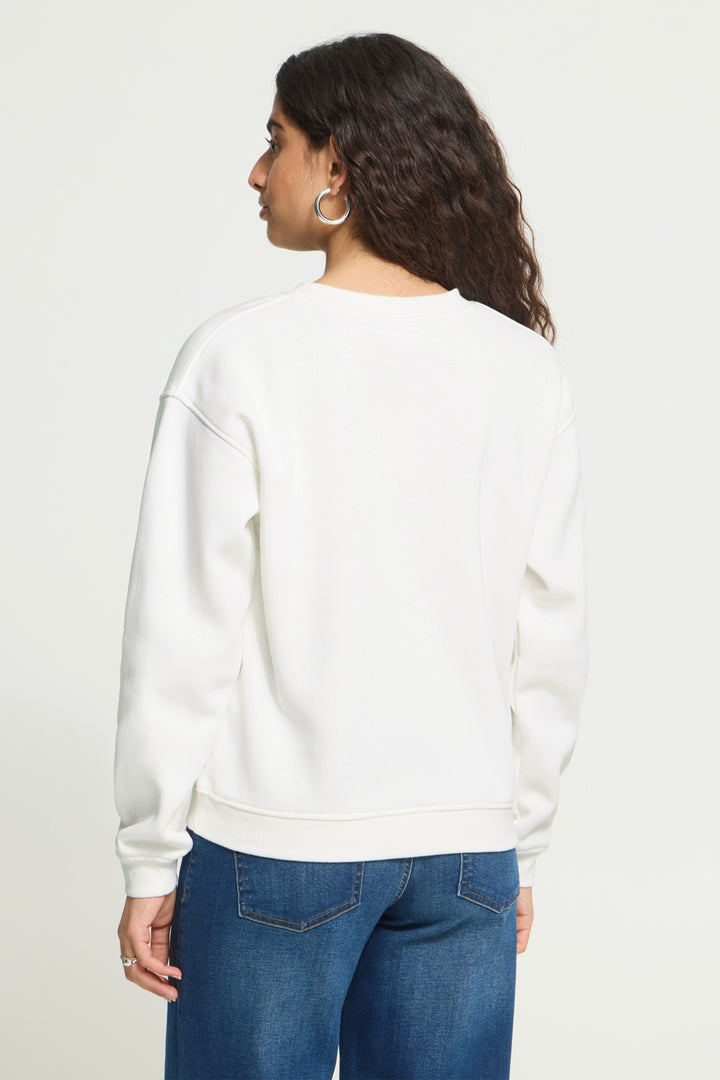 A woman shown from the back wearing a white crewneck sweatshirt and blue jeans against a plain light background.