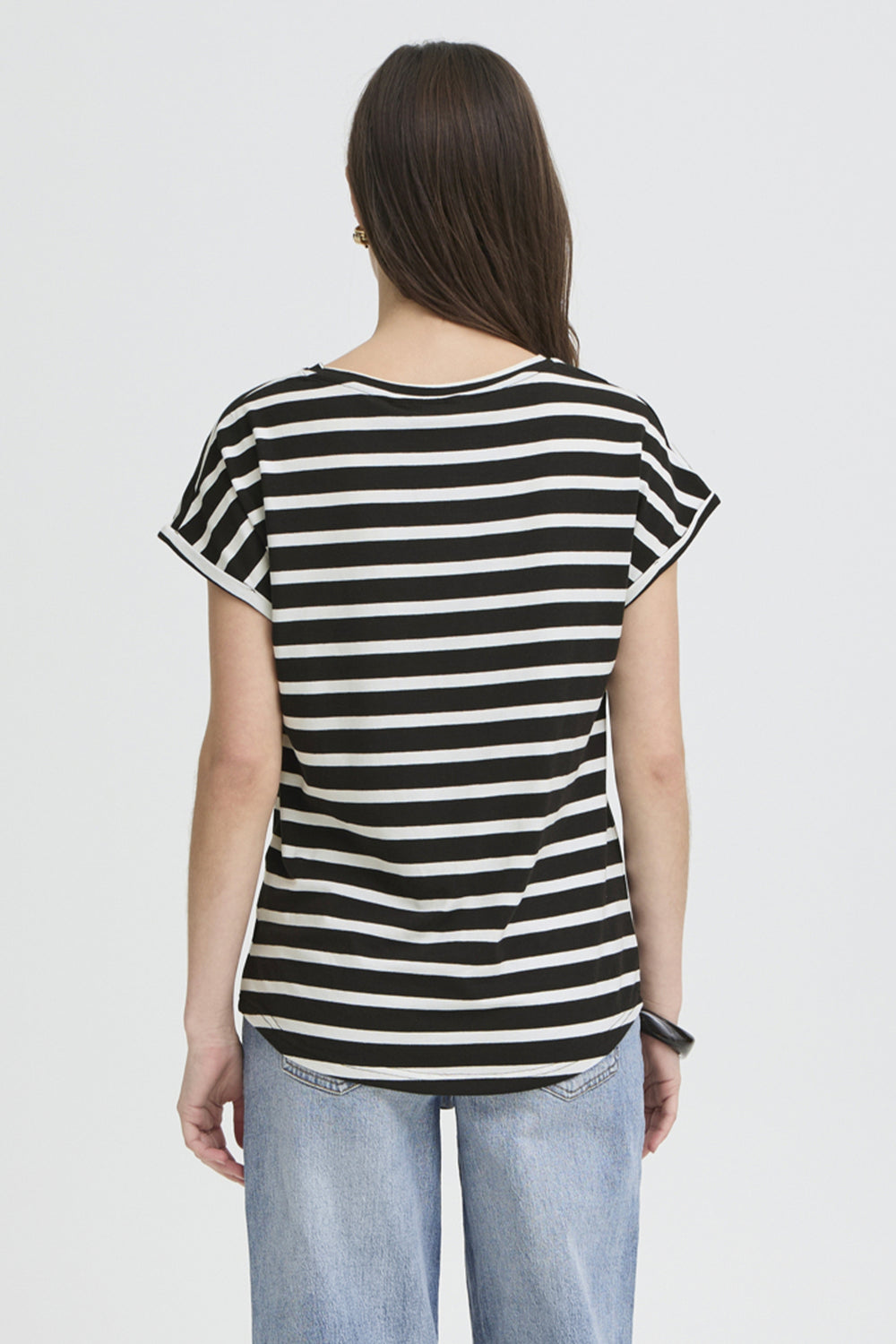 A woman viewed from the back wearing a black and white horizontally striped short-sleeve t-shirt and light blue jeans, set against a plain light gray studio background.