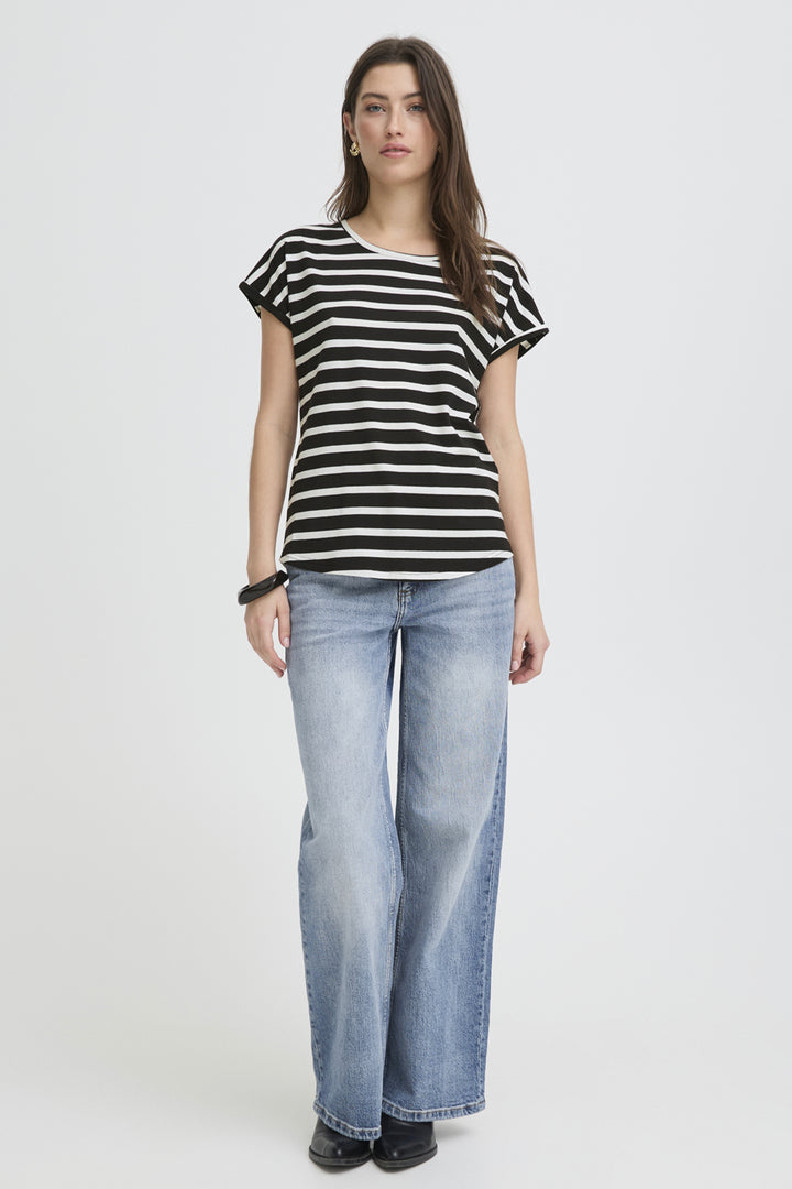 A woman modeling a black and white horizontally striped short-sleeve t-shirt with light-wash blue wide-leg jeans, standing against a plain light gray studio background.
