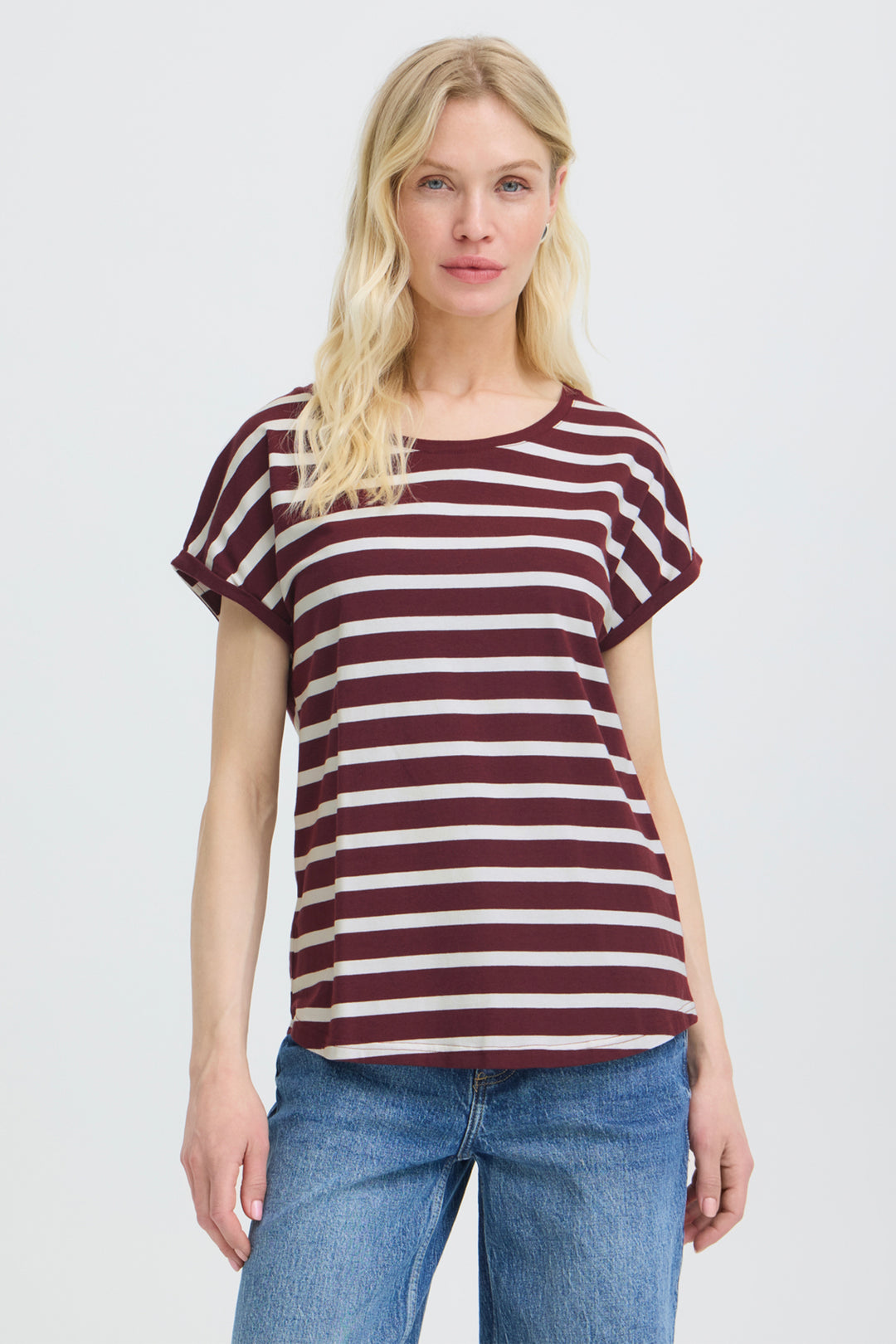 A woman modeling a short-sleeve crewneck t-shirt with horizontal burgundy and off-white stripes, paired with blue jeans, against a light gray studio background.