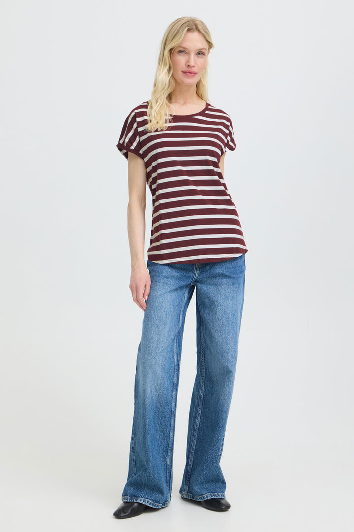 A woman modeling a short-sleeve crewneck t-shirt with horizontal burgundy and white stripes, paired with wide-leg blue jeans and black shoes, against a plain light gray studio background.