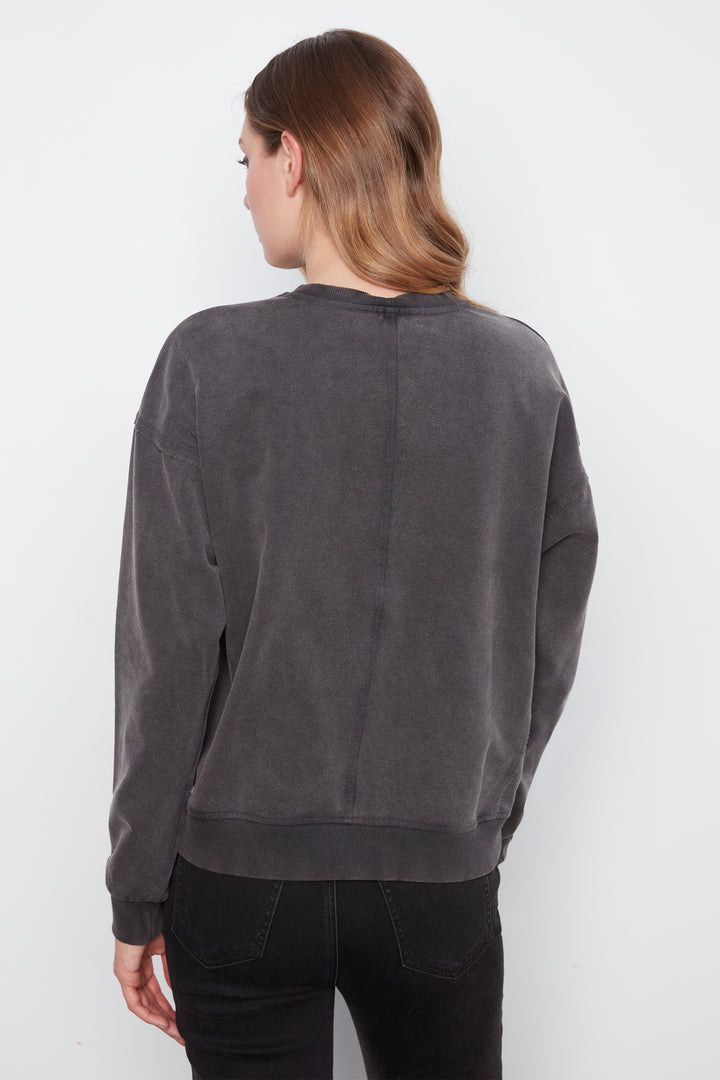 A woman shown from the back wearing a dark gray washed crewneck sweatshirt and black pants, photographed against a plain white studio background.