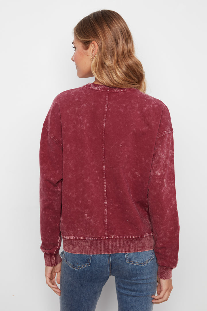 A woman viewed from the back wearing a washed, faded burgundy crewneck sweatshirt and blue jeans against a plain white background.