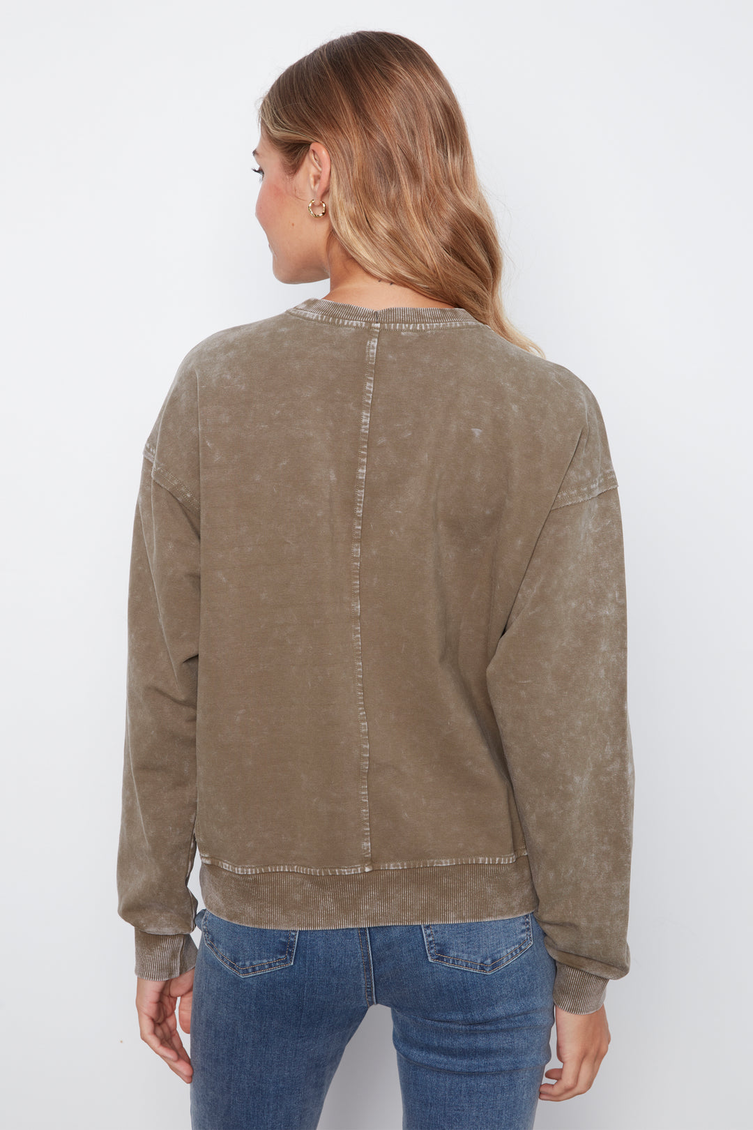 A woman shown from the back wearing a cropped, long-sleeve crewneck sweatshirt in a washed taupe-brown color, paired with blue jeans, against a plain white studio background.
