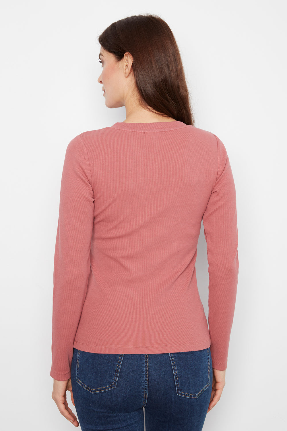 A woman shown from the back wearing a dusty rose long-sleeve top and dark blue jeans against a plain white background.